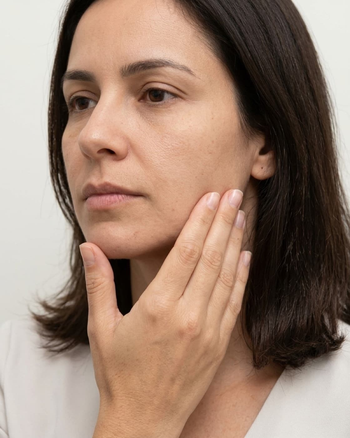 Mulher com a mão sobre o ângulo da mandíbula, na região do músculo masseter