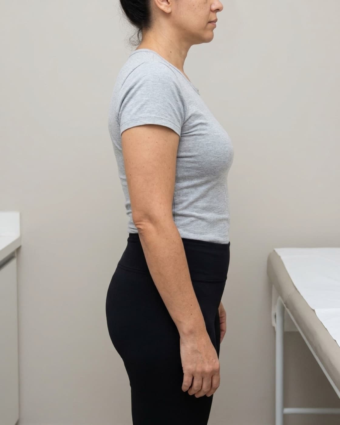 Mulher de perfil vestindo legging e camiseta, em pé no consultório